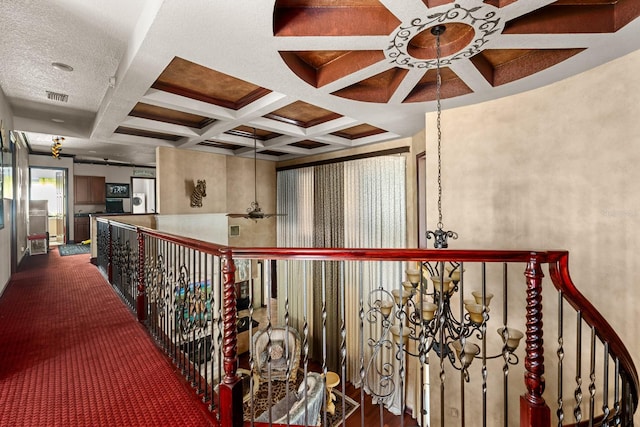 corridor with coffered ceiling, a notable chandelier, beam ceiling, and dark carpet