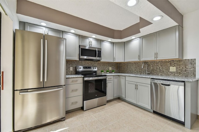 kitchen featuring decorative backsplash, appliances with stainless steel finishes, a textured ceiling, sink, and light stone counters