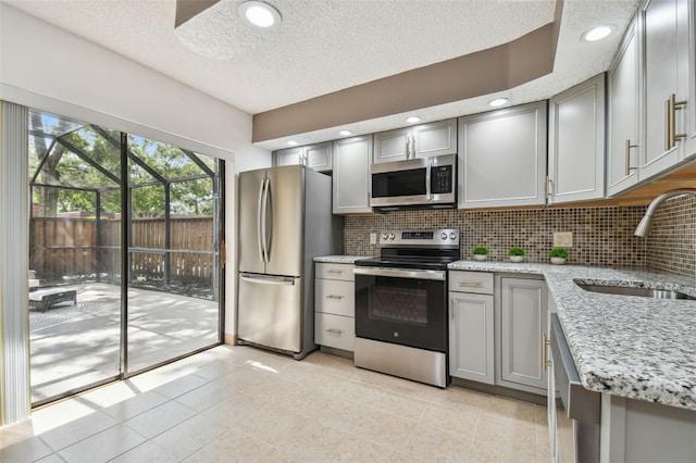 kitchen with appliances with stainless steel finishes, light stone countertops, sink, and gray cabinets