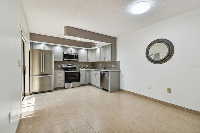 kitchen featuring decorative backsplash, a textured ceiling, sink, gray cabinetry, and stainless steel appliances