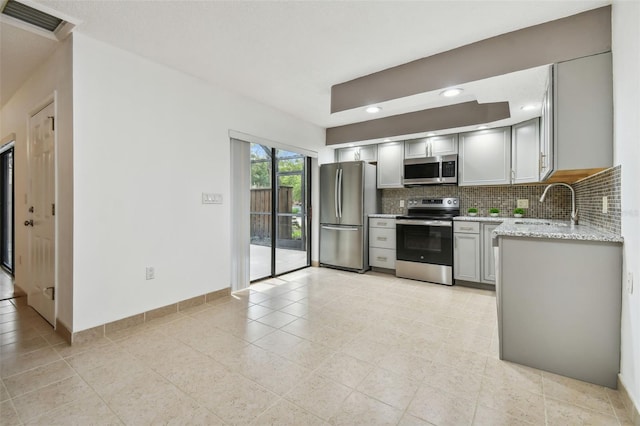 kitchen featuring decorative backsplash, light stone countertops, sink, gray cabinetry, and stainless steel appliances