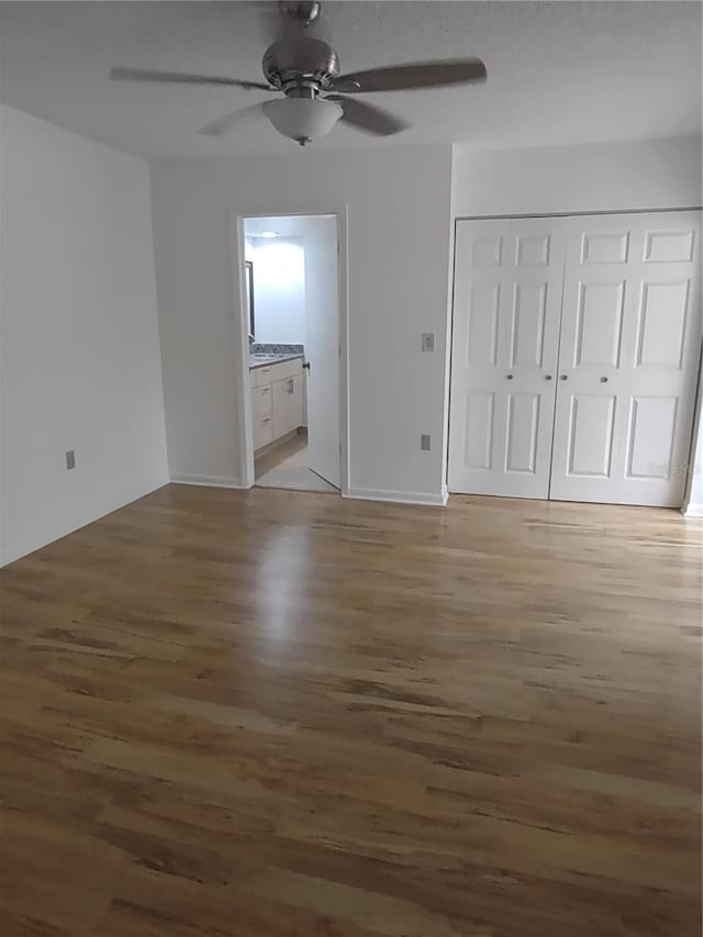 unfurnished bedroom with ensuite bath, dark wood-type flooring, a closet, and ceiling fan