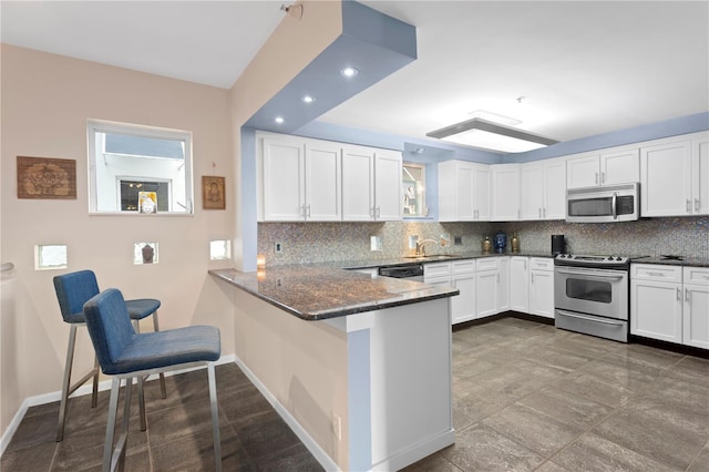 kitchen with tasteful backsplash, kitchen peninsula, white cabinets, and appliances with stainless steel finishes