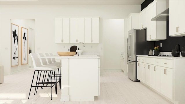 kitchen with white cabinets, an island with sink, light hardwood / wood-style flooring, wall chimney range hood, and a kitchen bar