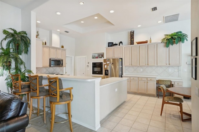 kitchen with kitchen peninsula, a raised ceiling, appliances with stainless steel finishes, a kitchen breakfast bar, and light tile patterned flooring