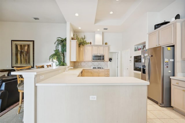 kitchen with kitchen peninsula, stainless steel appliances, a kitchen bar, light tile patterned floors, and tasteful backsplash