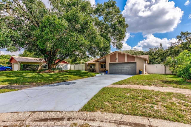 mid-century modern home featuring stucco siding, concrete driveway, an attached garage, a front yard, and fence