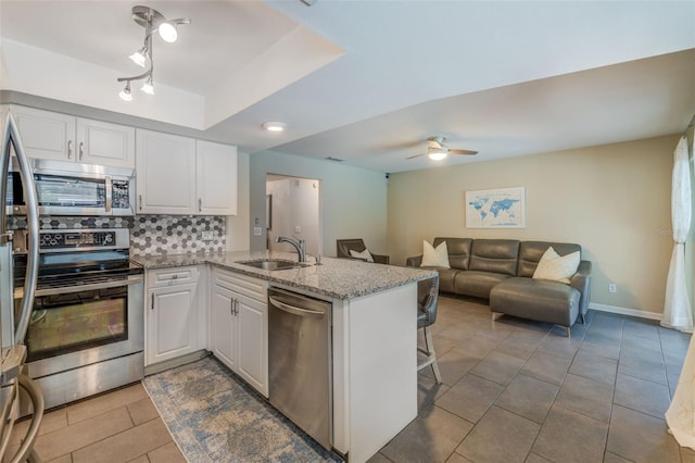 kitchen featuring decorative backsplash, white cabinets, appliances with stainless steel finishes, a peninsula, and a sink