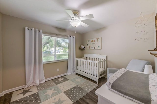 bedroom featuring a ceiling fan, a crib, baseboards, and wood finished floors