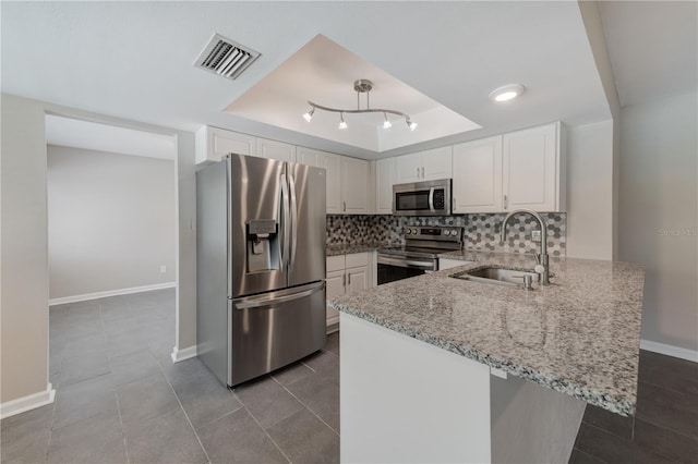 kitchen with stainless steel appliances, a peninsula, a sink, visible vents, and a tray ceiling