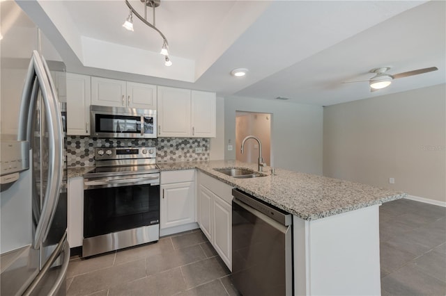 kitchen with a raised ceiling, decorative backsplash, appliances with stainless steel finishes, a sink, and a peninsula