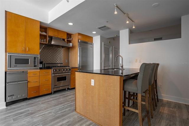 kitchen with kitchen peninsula, built in appliances, light wood-type flooring, range hood, and sink