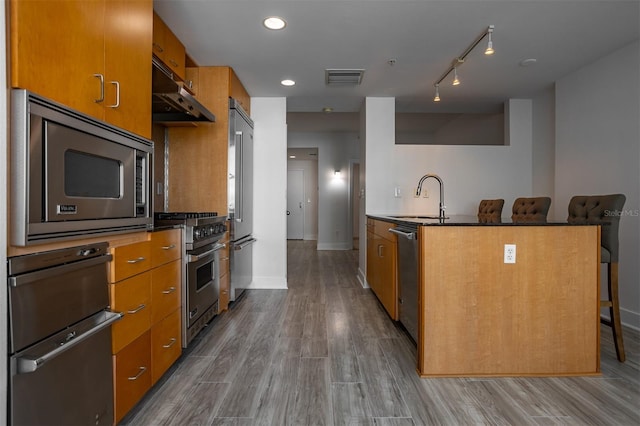 kitchen with hardwood / wood-style flooring, premium appliances, sink, and a breakfast bar