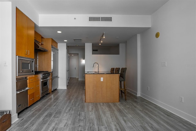 kitchen with dark hardwood / wood-style floors, premium appliances, sink, and a breakfast bar