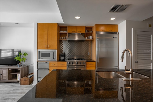 kitchen featuring sink, light hardwood / wood-style flooring, built in appliances, range hood, and dark stone counters