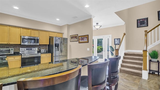 kitchen with appliances with stainless steel finishes, a kitchen breakfast bar, dark stone countertops, crown molding, and decorative backsplash