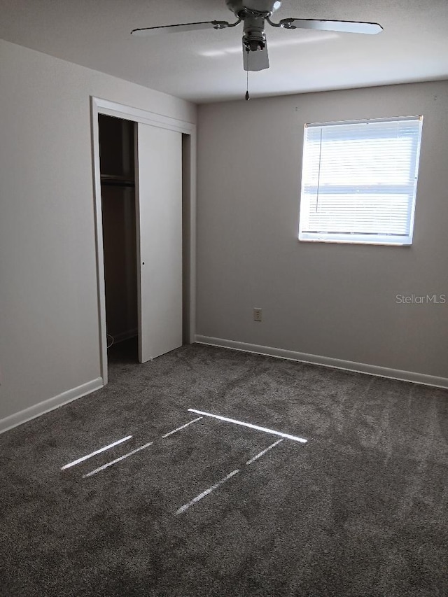 unfurnished bedroom with ceiling fan, a closet, and dark colored carpet