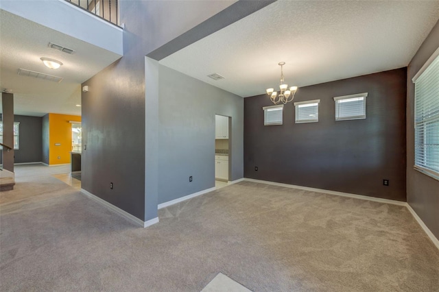 spare room featuring light carpet, an inviting chandelier, and a textured ceiling