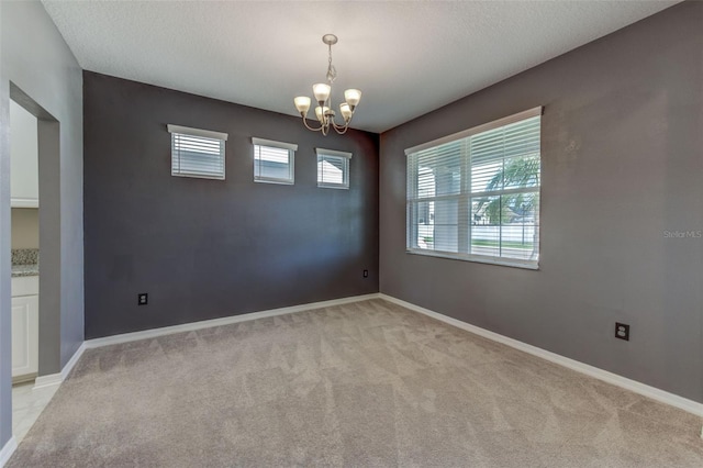 spare room featuring a chandelier, a textured ceiling, and light carpet