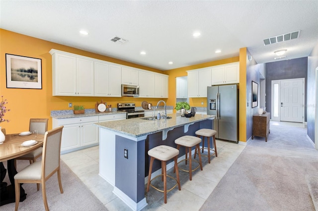 kitchen with light stone countertops, white cabinets, stainless steel appliances, sink, and a center island with sink