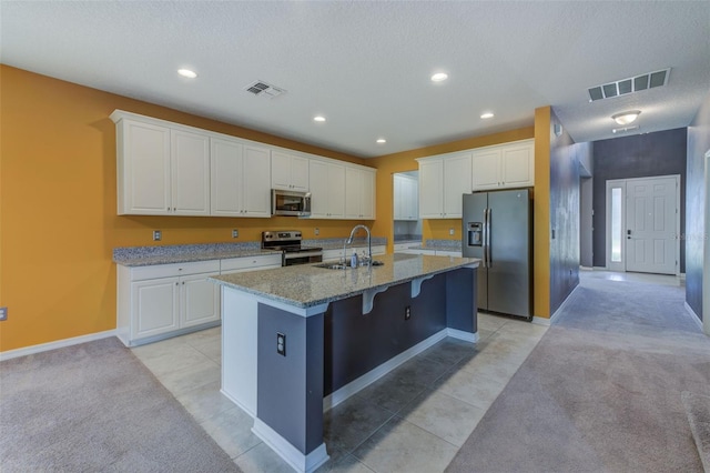 kitchen with white cabinets, stainless steel appliances, light stone counters, and a kitchen island with sink