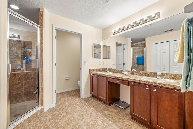 bathroom featuring vanity, a textured ceiling, toilet, and a shower with door