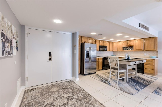 kitchen with a center island, light tile patterned flooring, tasteful backsplash, a kitchen breakfast bar, and black appliances