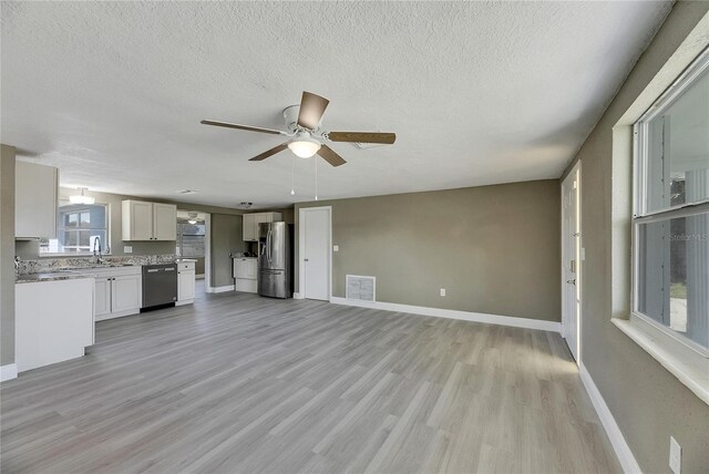 interior space with a textured ceiling, ceiling fan, light hardwood / wood-style flooring, and a wealth of natural light