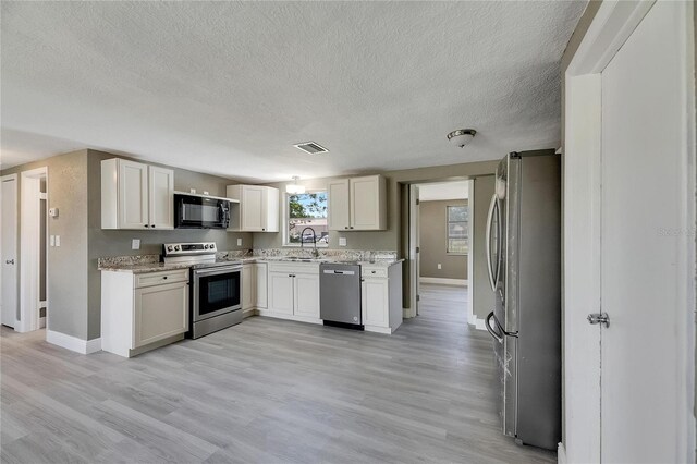 kitchen with a textured ceiling, sink, light hardwood / wood-style flooring, and stainless steel appliances