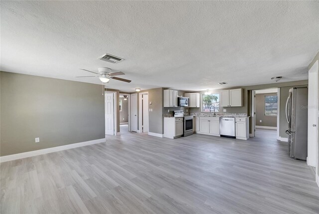 unfurnished living room featuring ceiling fan, a textured ceiling, light wood-type flooring, and sink