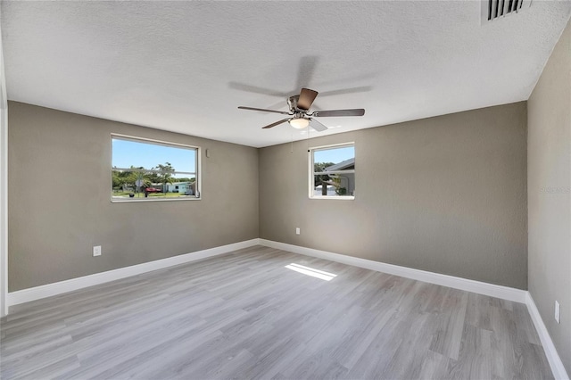 spare room featuring a textured ceiling, light hardwood / wood-style floors, ceiling fan, and plenty of natural light