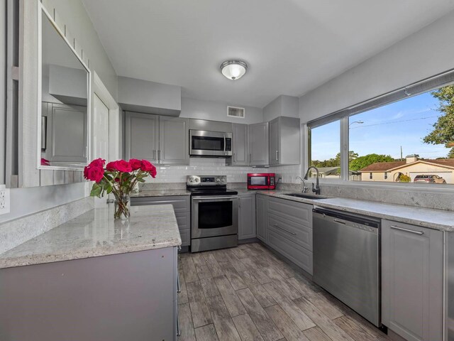 kitchen with light stone counters, sink, gray cabinets, appliances with stainless steel finishes, and light wood-type flooring