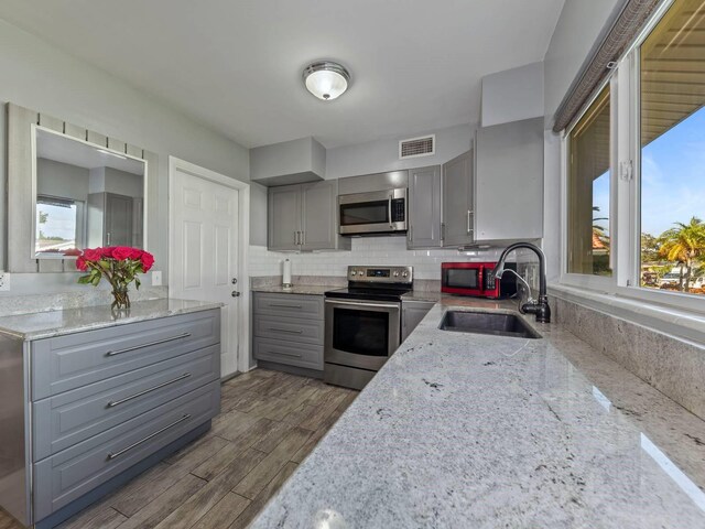 kitchen with dark hardwood / wood-style floors, sink, gray cabinetry, stainless steel appliances, and light stone countertops