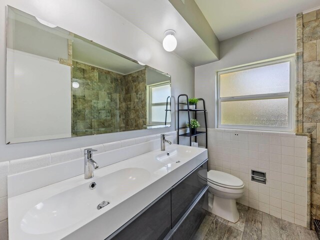 bathroom with a tile shower, tile walls, hardwood / wood-style floors, vanity, and toilet