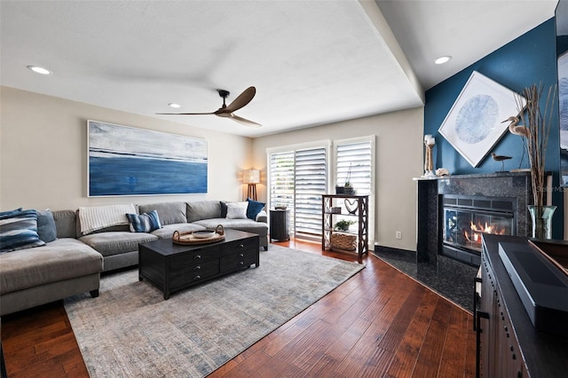 living room featuring dark hardwood / wood-style flooring, ceiling fan, and a premium fireplace