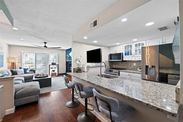 kitchen with a breakfast bar, light stone counters, white cabinets, kitchen peninsula, and dark hardwood / wood-style flooring