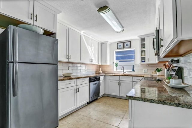 kitchen featuring white cabinets, stainless steel appliances, dark stone counters, and light tile patterned flooring