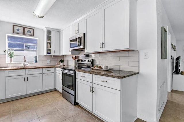 kitchen with appliances with stainless steel finishes, tasteful backsplash, sink, dark stone countertops, and white cabinetry