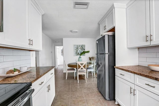 kitchen featuring stainless steel appliances, light tile patterned floors, dark stone countertops, decorative backsplash, and white cabinets