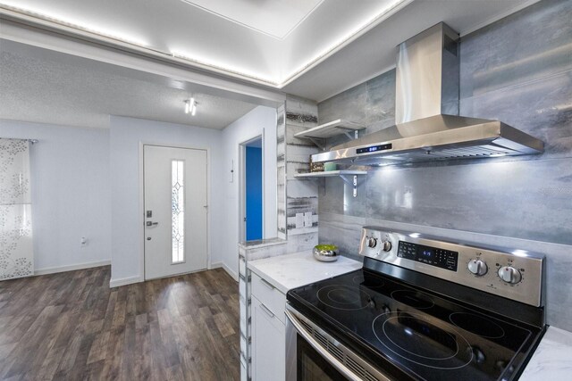 kitchen with dark wood-type flooring, electric stove, wall chimney exhaust hood, a textured ceiling, and white cabinetry