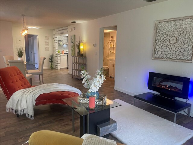 living area with a glass covered fireplace, visible vents, baseboards, and wood finished floors