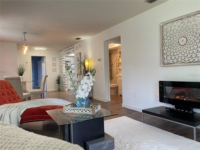 living room featuring baseboards, visible vents, a glass covered fireplace, wood finished floors, and a textured ceiling