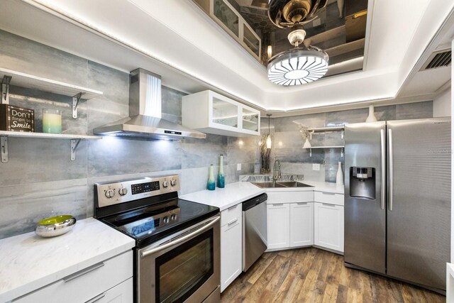 kitchen featuring dark wood-type flooring, wall chimney range hood, sink, white cabinetry, and stainless steel appliances