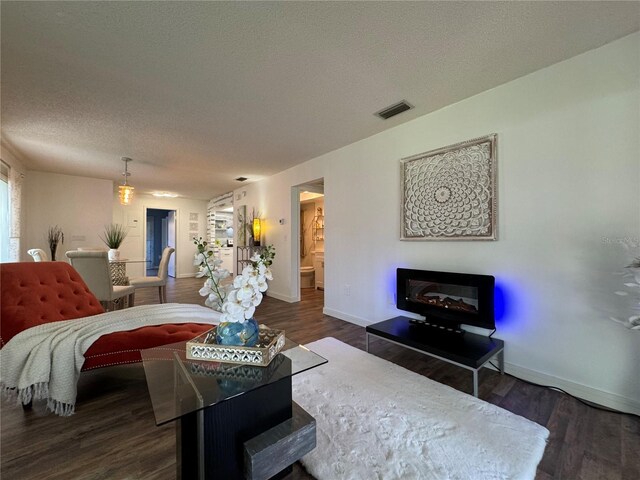 bedroom featuring a textured ceiling, wood finished floors, visible vents, baseboards, and a glass covered fireplace