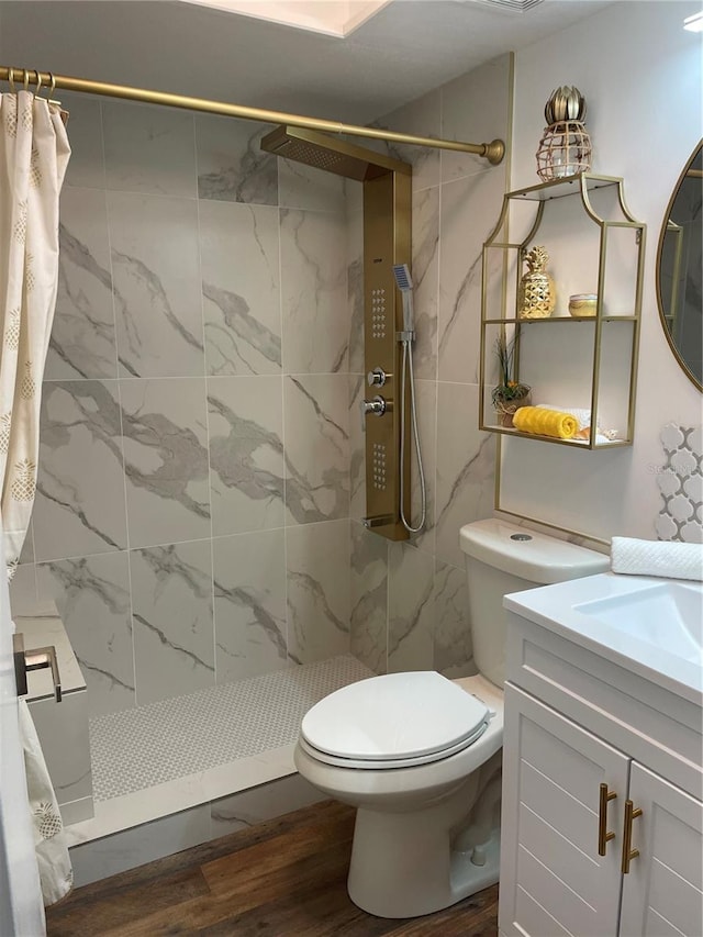 full bath featuring toilet, a tile shower, wood finished floors, and vanity