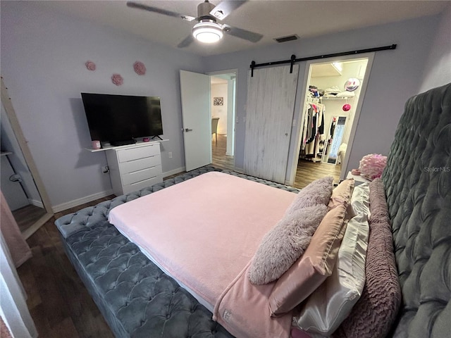 bedroom with a walk in closet, ceiling fan, a barn door, wood-type flooring, and a closet