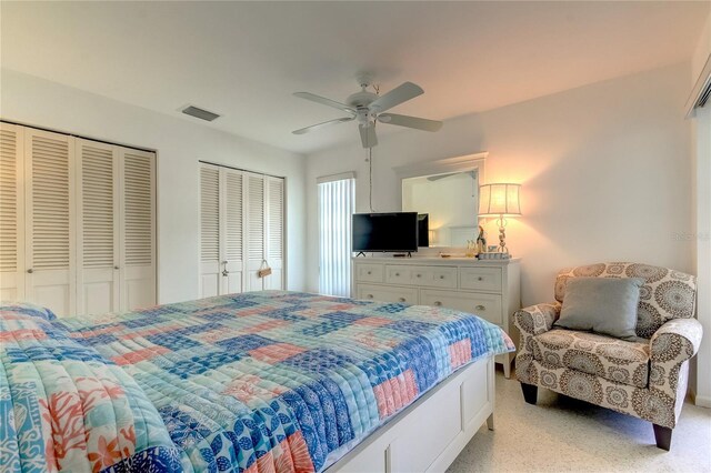 bedroom with ceiling fan, light colored carpet, and two closets