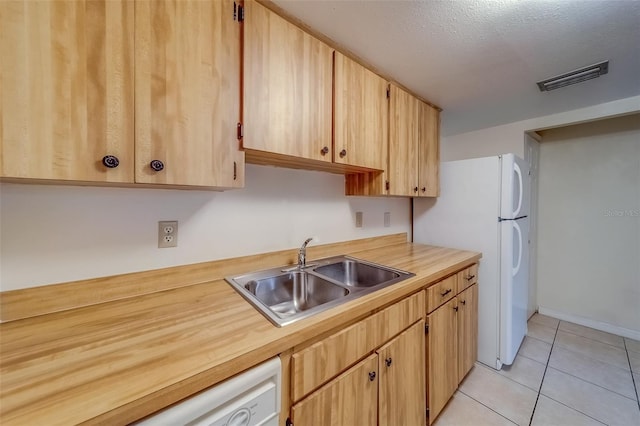 kitchen featuring a textured ceiling, light tile patterned flooring, sink, white appliances, and light brown cabinetry