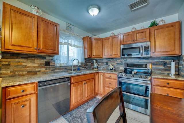 kitchen with backsplash, light stone counters, stainless steel appliances, sink, and light tile patterned flooring