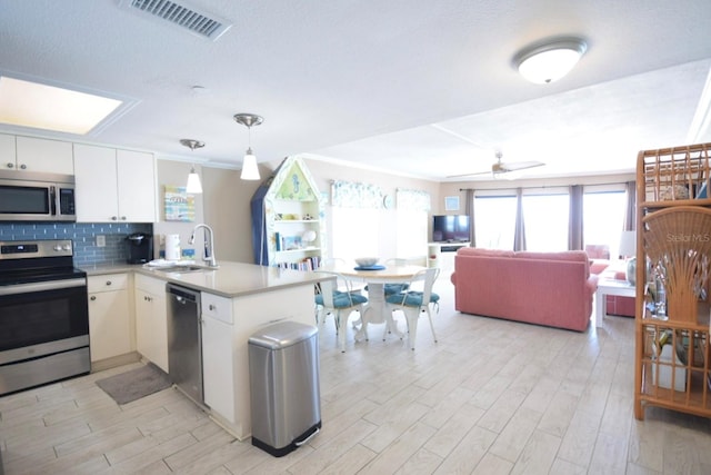 kitchen with sink, stainless steel appliances, kitchen peninsula, decorative light fixtures, and white cabinets